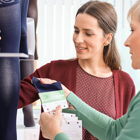 Two women looking at fabric swatches in a store setting for the bauerfeinds medical VenoTrain Micro in color navy