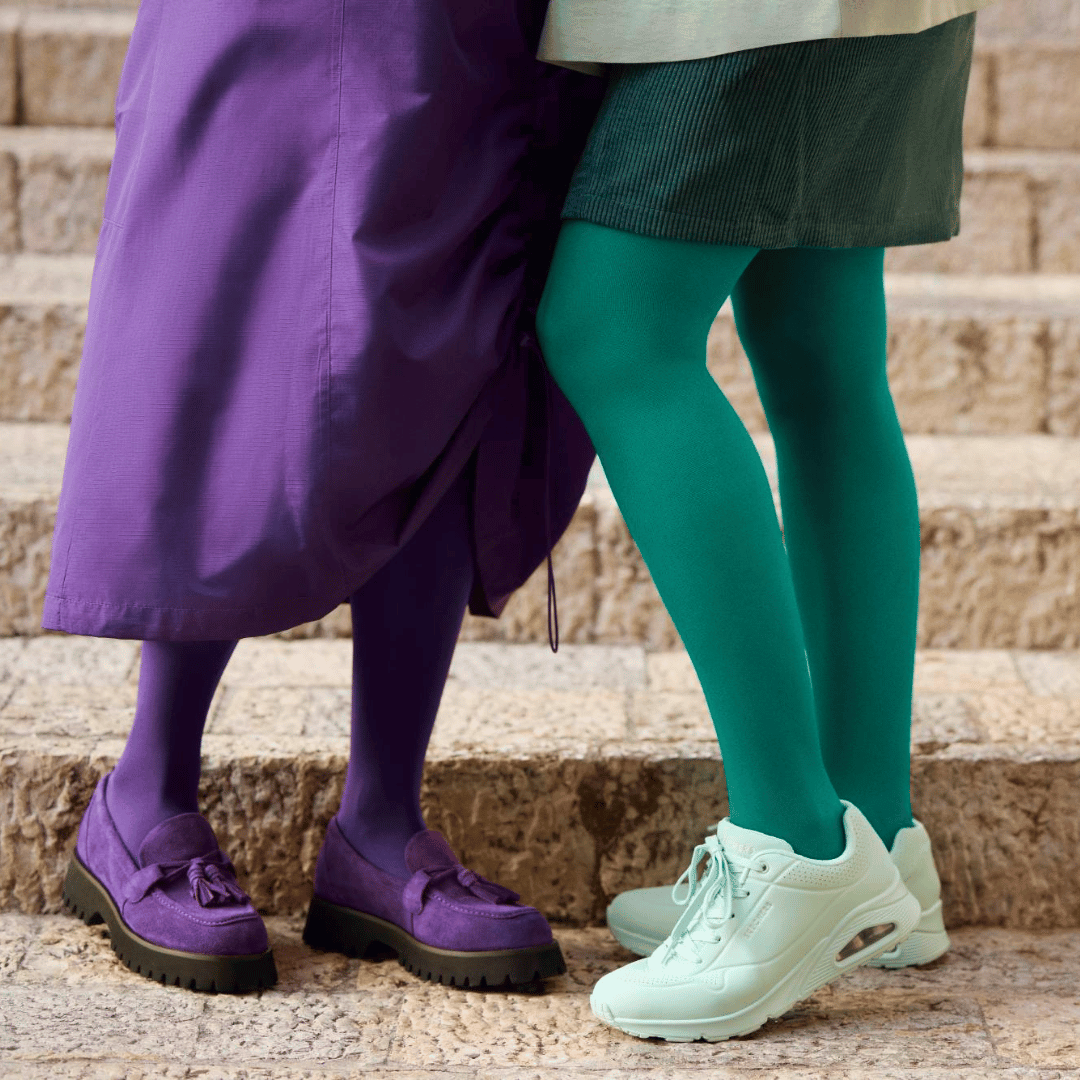 Two people wearing the bauerfeind medical venotrain soft compression stockings in colors french lavender, and irish green on stone steps.