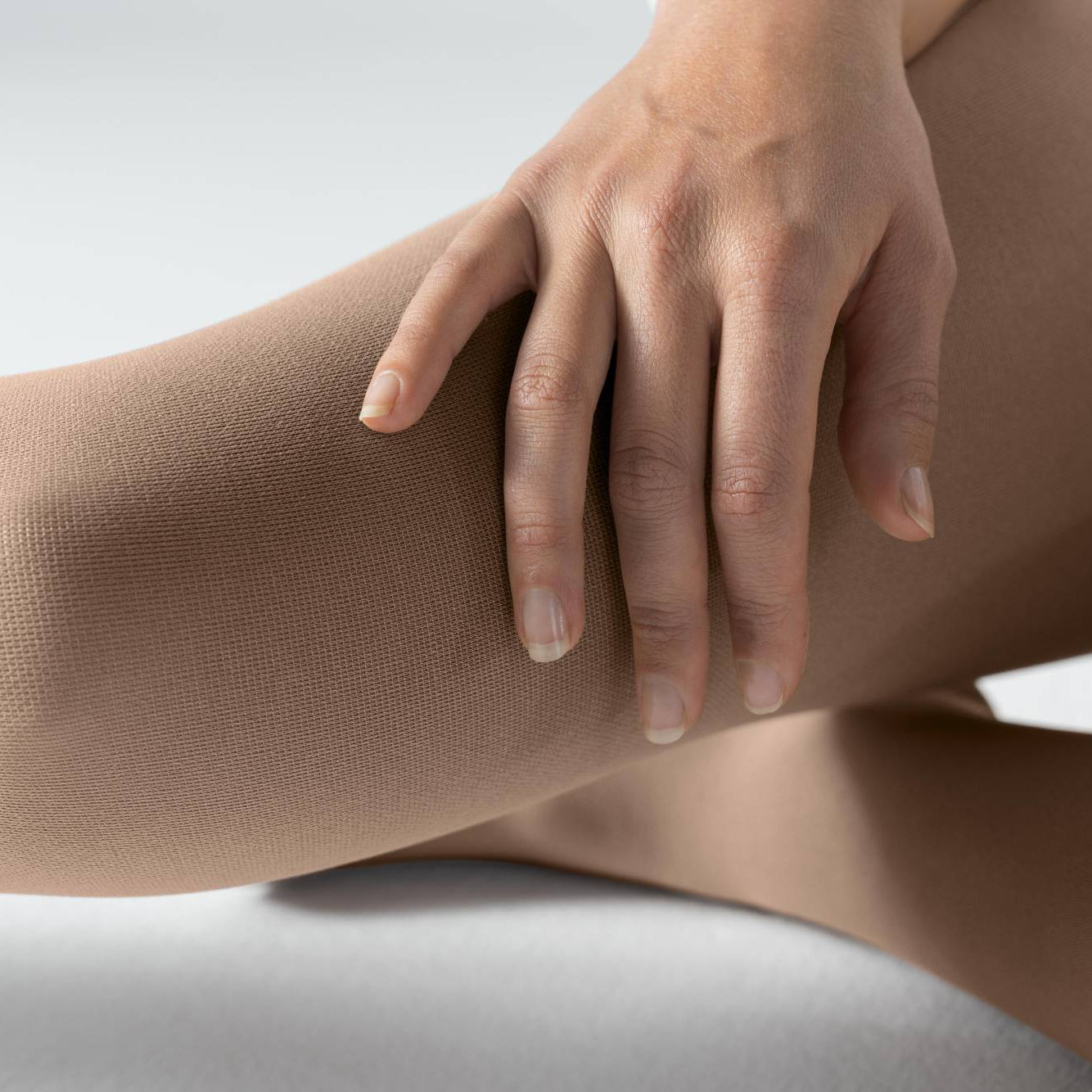 Close-up of a hand touching a leg wearing bauerfeinds medical Venotrain soft compression stockings color amaretto on a light background